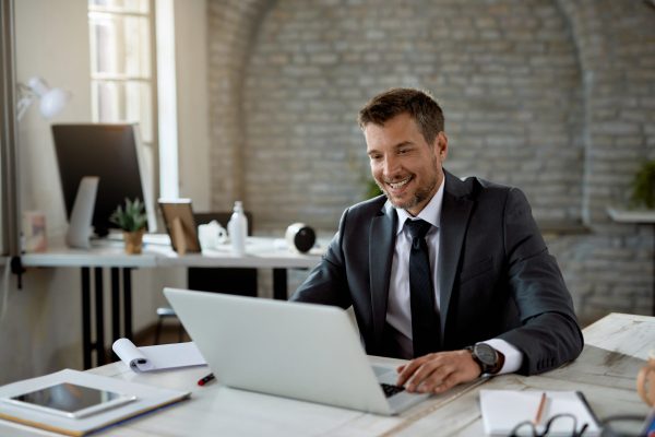 A happy male entrepreneur reading an email on his laptop while working in the office.